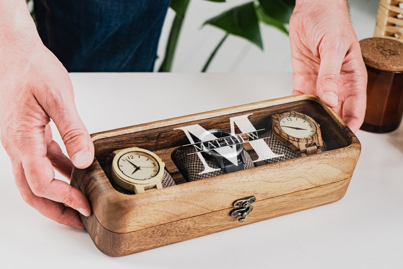 Unique Wood watch box for watches, featuring rounded corners, a sleek, treated wood texture, and a glass lid for constant visibility. Customize the glass lid with your own engraving.