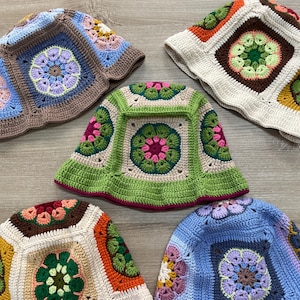 Könnte beinhalten: Fünf gehäkelte Bucket-Hats in verschiedenen Farben und Mustern. Die Hüte sind mit einem Granny-Square-Stich gearbeitet und haben florale Motive in Braun-, Grün-, Blau-, Rosa- und Gelbtönen.