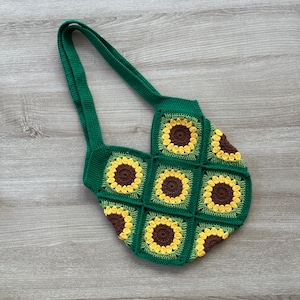 May include: Green crocheted tote bag with a sunflower pattern. The bag has two straps and is made of a thick yarn.