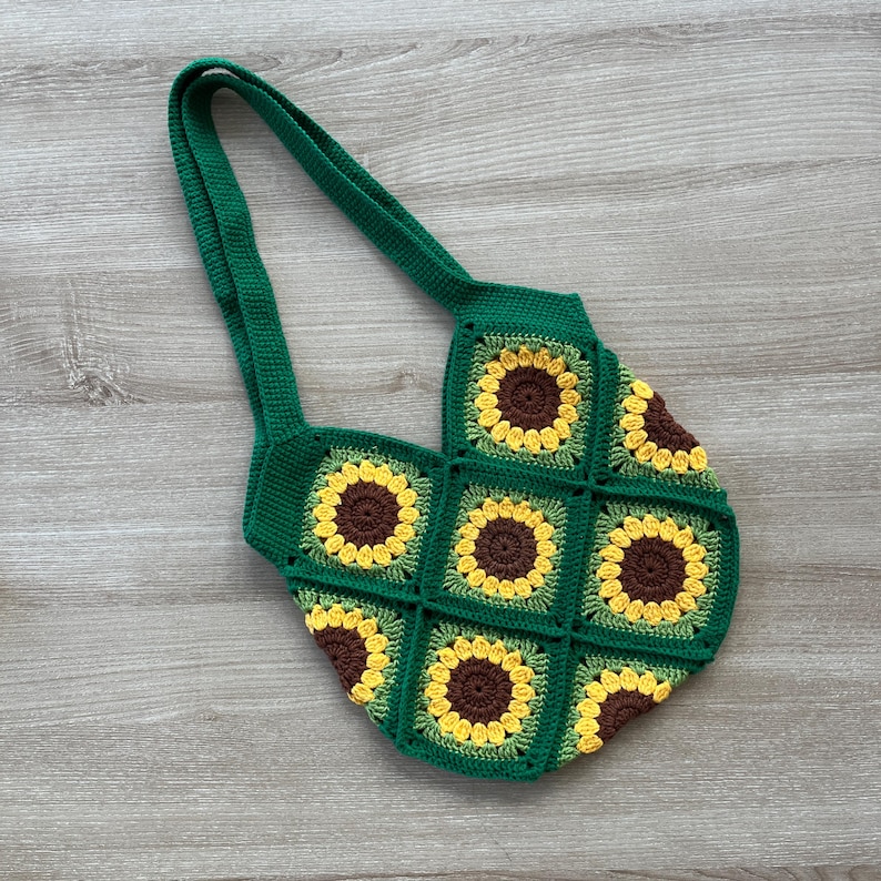 May include: Green crocheted tote bag with a sunflower pattern. The bag has two straps and is made of a thick yarn.