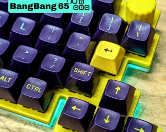 May include: A 65% mechanical keyboard with a yellow and purple color scheme. The keyboard has a teal accent around the edges and a yellow knob on the top right corner. The keyboard has the text "BangBang 65" printed on the top row.