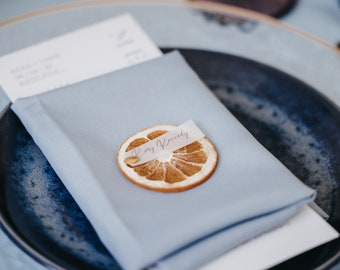 May include: A blue napkin with a dried orange slice on top. The orange slice has a small white tag with the name "Ray Kennedy" written on it.