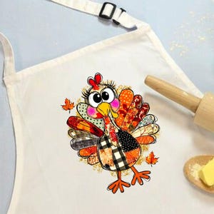 May include: White apron with a colorful cartoon turkey design. The turkey has a patchwork pattern of orange, black, and brown. The apron also features a wooden rolling pin, a small bowl with eggs, and a wooden spoon with butter.