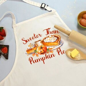 May include: White kitchen apron with a red and orange graphic of pumpkin pie and the text "Sweeter Than Pumpkin Pie".