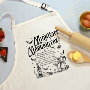 Może przedstawiać: Biały fartuch kuchenny z czarno-białą ilustracją przepisu na koktajl "Midnight Margaritas". Przepis zawiera listę składników i instrukcje, a także rysunek szklanki do koktajlu, butelki alkoholu i innych składników.