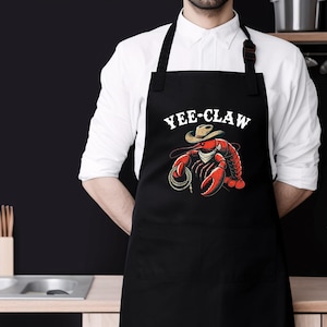 May include: Black apron featuring a red lobster wearing a cowboy hat and the text "Yee-Claw".