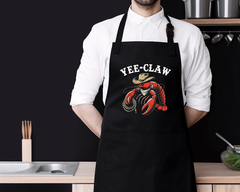 May include: Black apron featuring a red lobster wearing a cowboy hat and the text "Yee-Claw".