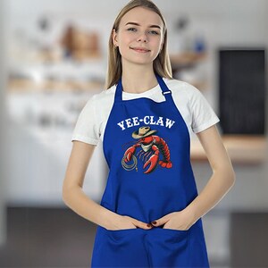 May include: A blue apron with a white graphic of a lobster wearing a cowboy hat and the text "YEE-CLAW".