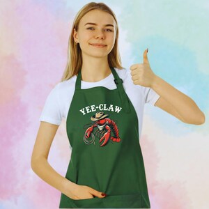 May include: Green apron featuring a cartoon lobster wearing a cowboy hat with the text "Yee-Claw".
