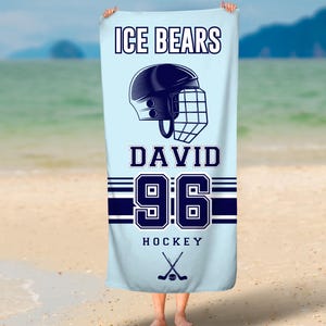 May include: A light blue beach towel with the text "ICE BEARS DAVID 96 HOCKEY" and a hockey helmet graphic. Two crossed hockey sticks are below the text.