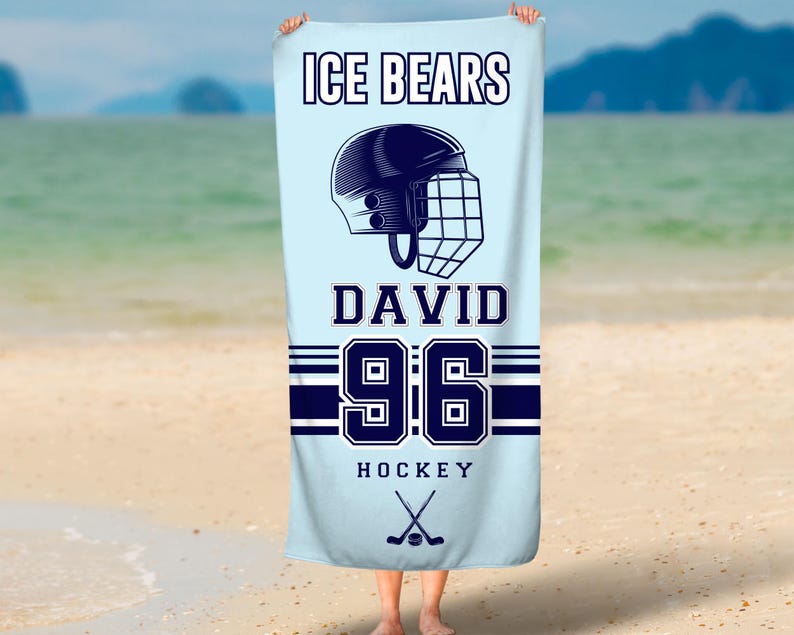 May include: A light blue beach towel with the text "ICE BEARS DAVID 96 HOCKEY" and a hockey helmet graphic. Two crossed hockey sticks are below the text.