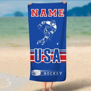 May include: A blue beach towel with a hockey player graphic, the words "NAME USA HOCKEY" and red and white stripes.