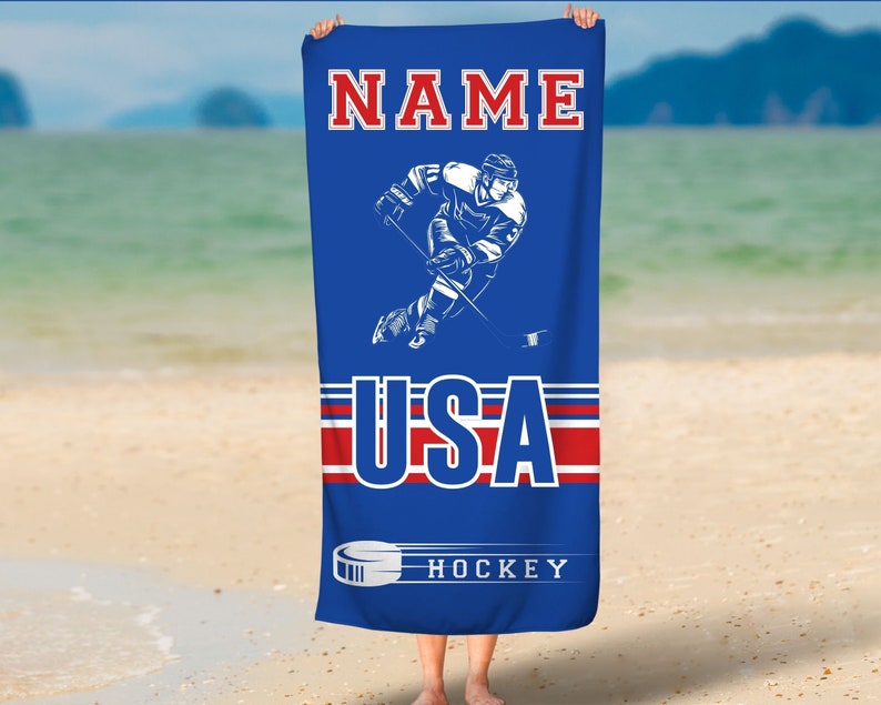 May include: A blue beach towel with a hockey player graphic, the words "NAME USA HOCKEY" and red and white stripes.