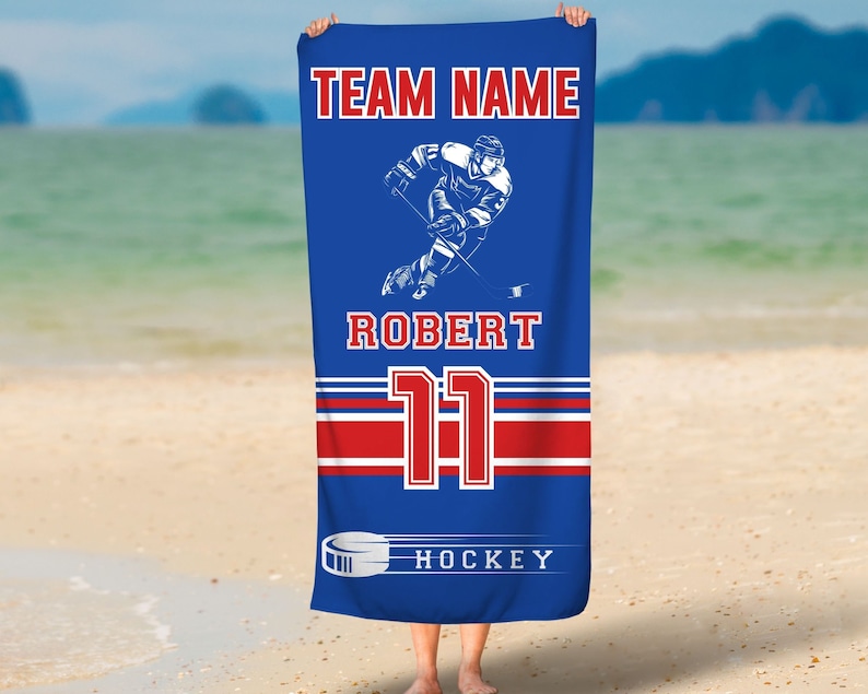 May include: Blue beach towel with a hockey player graphic, the text "TEAM NAME", "ROBERT", "11", and "HOCKEY", and red and white stripes.