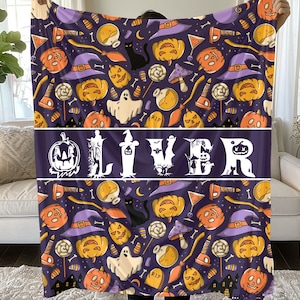 May include: A Halloween-themed blanket with a repeating pattern of pumpkins, witch hats, ghosts, and candy on a dark purple background. The name "OLIVER" is displayed in white block letters across the center of the blanket.
