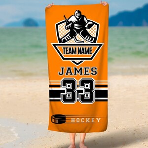 May include: Orange beach towel with a black hockey player graphic, the text "TEAM NAME", "JAMES", "33", and "HOCKEY".