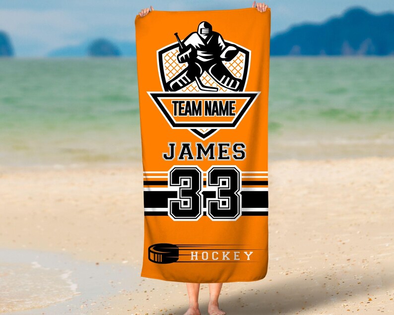 May include: Orange beach towel with a black hockey player graphic, the text "TEAM NAME", "JAMES", "33", and "HOCKEY".