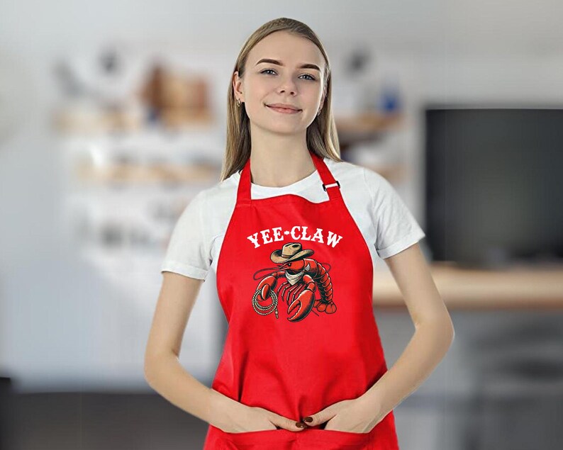 May include: Red kitchen apron with a white graphic of a lobster wearing a cowboy hat and the text "Yee-Claw".