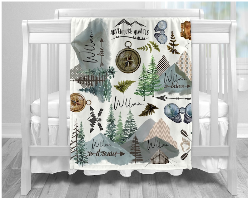 Pu&ograve; includere: Una copertina per neonati bianca con un tema boschivo. La copertina presenta un motivo ripetitivo di montagne, alberi, bussole, binocoli e frecce. Il testo "Adventure Awaits" e il nome "William" sono ripetuti in tutto il design.