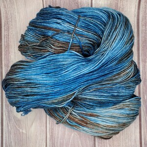May include: A skein of blue, brown, and gray yarn with a variegated color pattern. The yarn is wound into a loose ball shape.