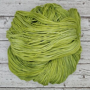 May include: A skein of green yarn with a variegated color pattern. The yarn is made of cotton and is soft to the touch.
