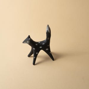 May include: A black ceramic fox figurine with white polka dots. The fox has a pointed snout, upright ears, and a tail with a white tip. The figurine is standing on four legs, with a minimalist design.