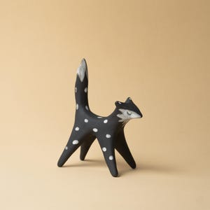 May include: A black ceramic fox figurine with white polka dots. The fox has a white-tipped tail and a white face with closed eyes. The figurine is standing on four legs and has a minimalist design.