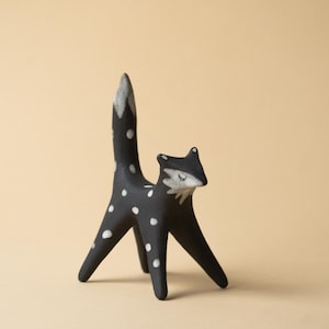 May include: A black fox ornament with white polka dots and a white-tipped tail. The fox has a stylized design with a slender body and legs. The fox's face is white with closed eyes, giving it a whimsical appearance.