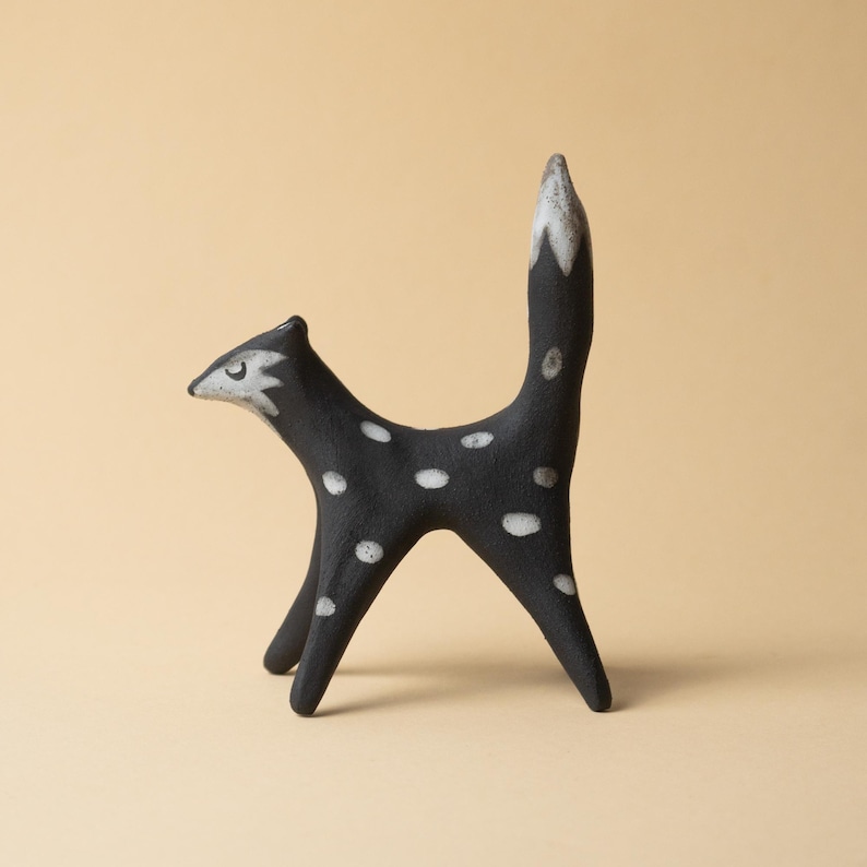 May include: A black ceramic fox ornament with white spots and a white-tipped tail. The fox has a distinctive design with a long, upright tail and a pointed snout. The ornament is a decorative item.