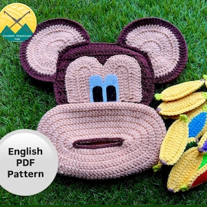 May include: Crocheted monkey-shaped tissue box cover with a matching set of bananas. The monkey has tan and brown details with blue eyes. The bananas are yellow with colorful tips. The image also includes the text "English PDF Pattern".