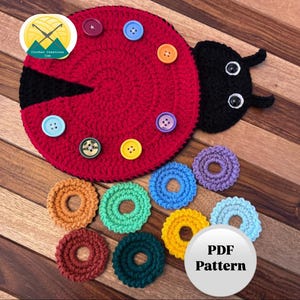 Könnte beinhalten: Ein roter gehäkelter Marienkäfer mit schwarzen Akzenten und Knopfaugen. Der Marienkäfer hat einen Kreis aus bunten Knöpfen auf seinem Rücken. Unter dem Marienkäfer befinden sich außerdem neun gehäkelte Kreise in verschiedenen Farben. Der Text "PDF Pattern" steht auf einem weißen Kreis.
