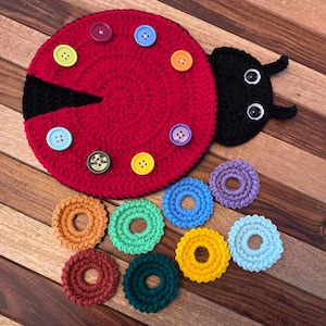 May include: A red crocheted ladybug with black accents and a black head with googly eyes. The ladybug has colorful buttons sewn on its body. There are also several colorful crocheted rings around the ladybug.