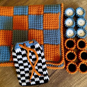 Könnte beinhalten: Eine gehäkelte Schachbrettdecke in Orange und Blau mit einer schwarz-weiß karierten Tasche und einem Satz gehäkelter Kreise in Weiß und Schwarz.