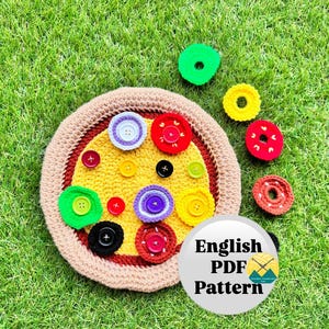 May include: A crocheted pizza with various button toppings, including red, green, yellow, and black. The pizza is surrounded by a tan crust and sits on a bed of green grass. Additional crocheted toppings are scattered around the pizza. The image includes a white circle with the text "English PDF Pattern".