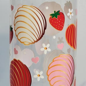 May include: Clear glass jar with a wooden lid, decorated with illustrations of strawberries, conchas, hearts, and flowers. The jar is cylindrical and appears to be empty.