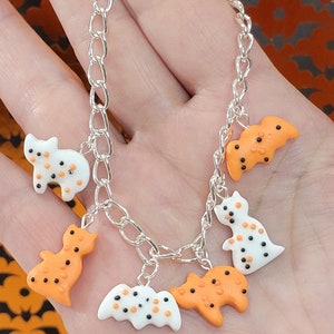 May include: A silver chain bracelet with five Halloween-themed charms. The charms are shaped like bats and ghosts and are decorated with orange and white icing and black sprinkles.