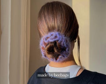 May include: A purple and brown crocheted hair bun wrap, worn at the nape of the neck. The hair accessory is made of a soft, fuzzy yarn. The text "made by beebags" is visible at the bottom of the image.