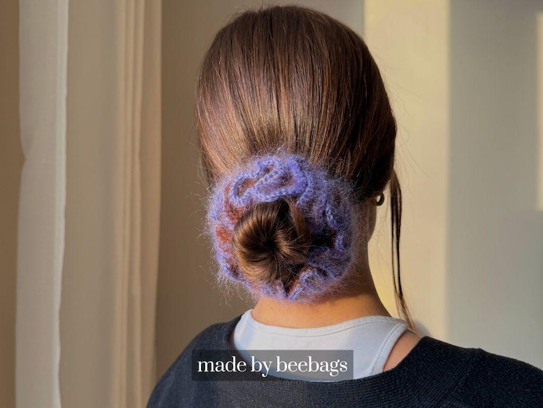 May include: A purple and brown crocheted hair bun wrap, worn at the nape of the neck. The hair accessory is made of a soft, fuzzy yarn. The text "made by beebags" is visible at the bottom of the image.