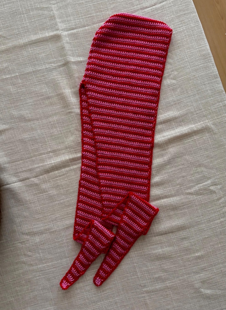 Puede incluir: Un conjunto de bufanda y calentadores de piernas a juego hechos a mano con ganchillo. El conjunto es rojo con rayas horizontales rosas. La bufanda es larga y rectangular, y los calentadores son tubulares.