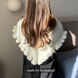 Peut inclure: Un châle en tricot triangulaire de couleur crème avec une texture douce et duveteuse et un bord à volants. Le vêtement est drapé sur les épaules et comporte le texte "made by beebagspl" imprimé en blanc au centre inférieur de l'image.