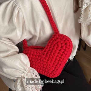 Può includere: Una borsa all'uncinetto a forma di cuore, di colore rosso brillante, con una lunga tracolla. La borsa è realizzata con filato spesso e ha un aspetto strutturato. Il testo "made by beebagspl" è visibile in basso nell'immagine.