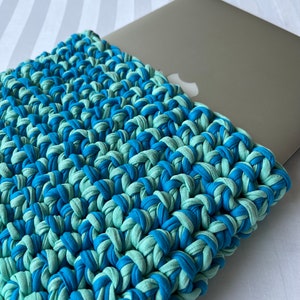 May include: A blue and green crocheted laptop sleeve. The sleeve is made of thick yarn and has a textured surface.