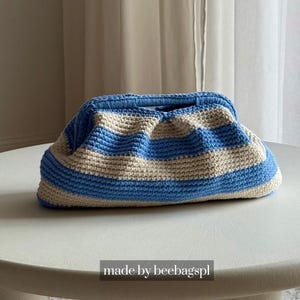 Könnte beinhalten: Eine rechteckige Häkeltasche mit horizontalen Streifen in Hellblau und Creme. Die Tasche hat eine strukturierte Rahmenöffnung an der Oberseite und eine geraffte, weiche Textur. Der Text "made by beebagspl" ist unten in der Mitte zu sehen.