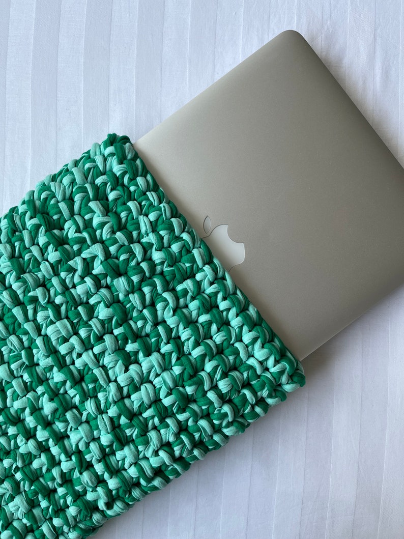 May include: A green and light green crocheted laptop sleeve with a laptop inside.