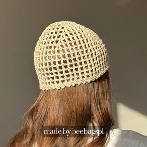 Op de afbeelding: Een beige gehaakte hoed met een netachtig patroon. De hoed wordt op het hoofd van een persoon gedragen, met lang bruin haar zichtbaar. De tekst "made by beebagspl" staat onderaan de afbeelding.