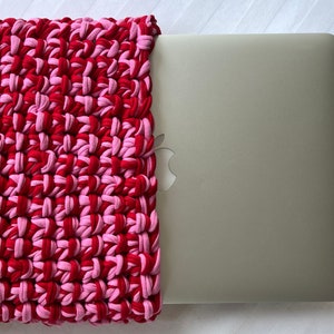May include: A red and pink crocheted laptop sleeve with a silver laptop inside.