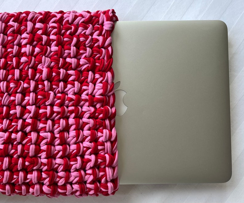 May include: A red and pink crocheted laptop sleeve with a silver laptop inside.