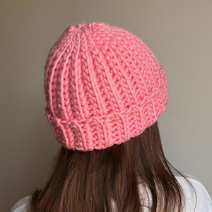 May include: A pink, ribbed knit beanie hat. The hat is made of a thick, soft yarn and has a classic, close-fitting design. The hat is a solid, vibrant pink color and is suitable for cold weather.