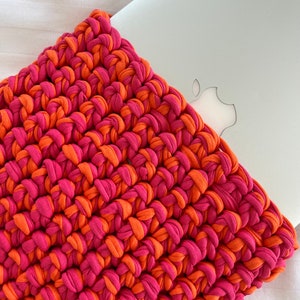 May include: A crocheted laptop sleeve in pink and orange. The sleeve is made with thick yarn and has a simple, textured design.