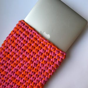 May include: A pink and orange crocheted laptop sleeve. The sleeve is made of thick yarn and has a simple, modern design.
